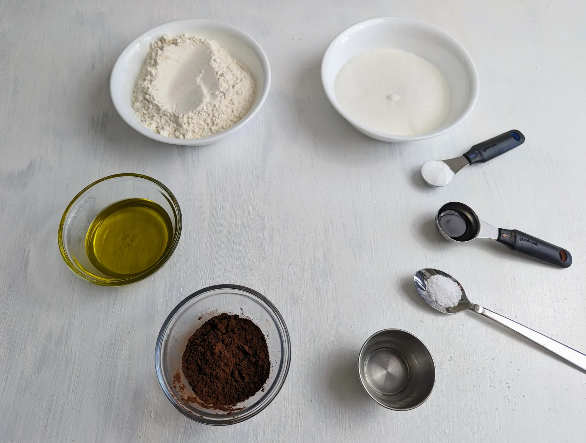 An image of the ingredients; flour, sugar, baking soda, vanilla, salt, vinegar, cocoa and olive oil