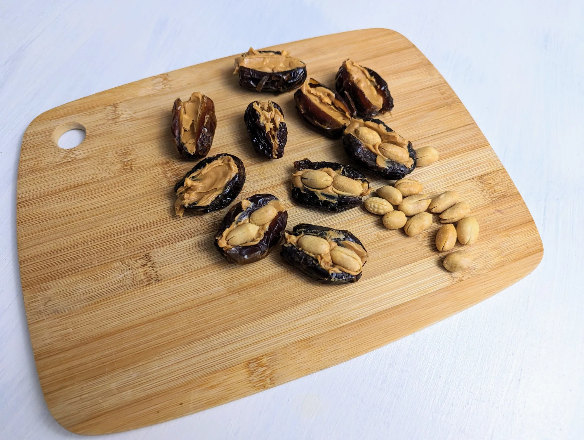 Pitted dates filled with peanut butter and peanuts on a cutting board