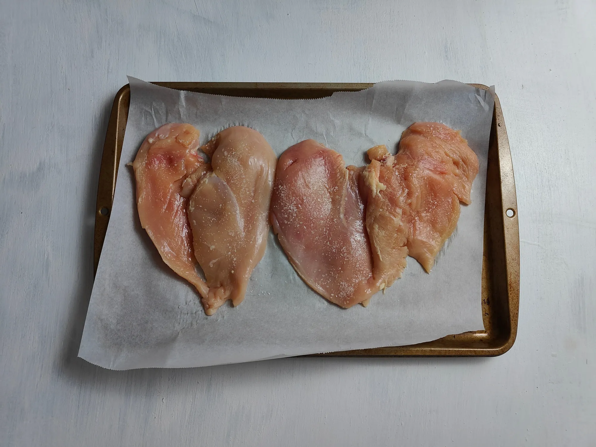 Butterflied chicken breast on a parchment lined sheet tray