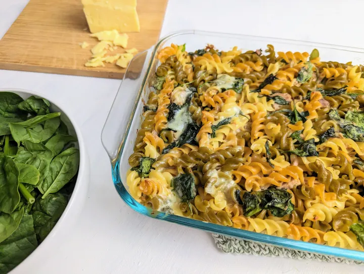 Rotini pasta, spinach, tuna and cheese in a casserole dish, next to spinach and cheese.
