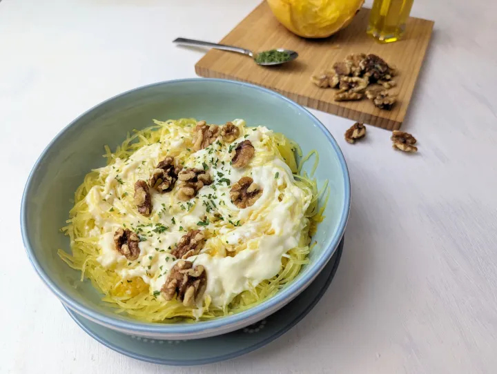 Spaghetti squash in a bowl with cheesy sauce, parsley and walnuts