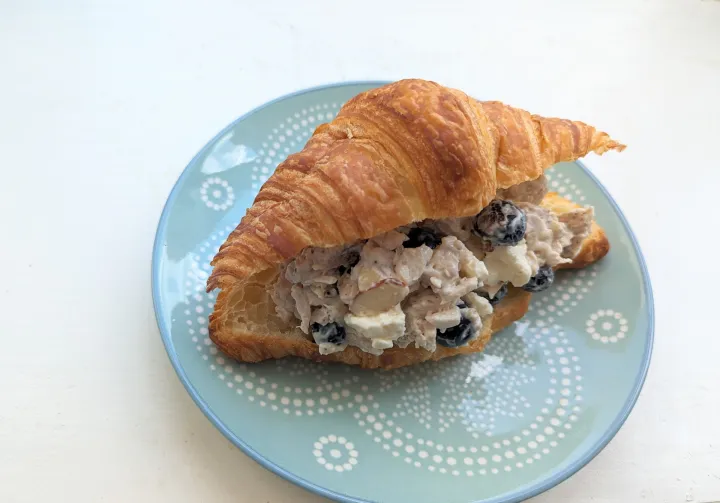 A croissant on a blue plate filled with chicken, almonds and blueberries