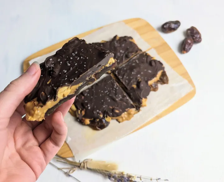 A piece of chocolate peanut butter date bark, with a cutting board that has more of it. 