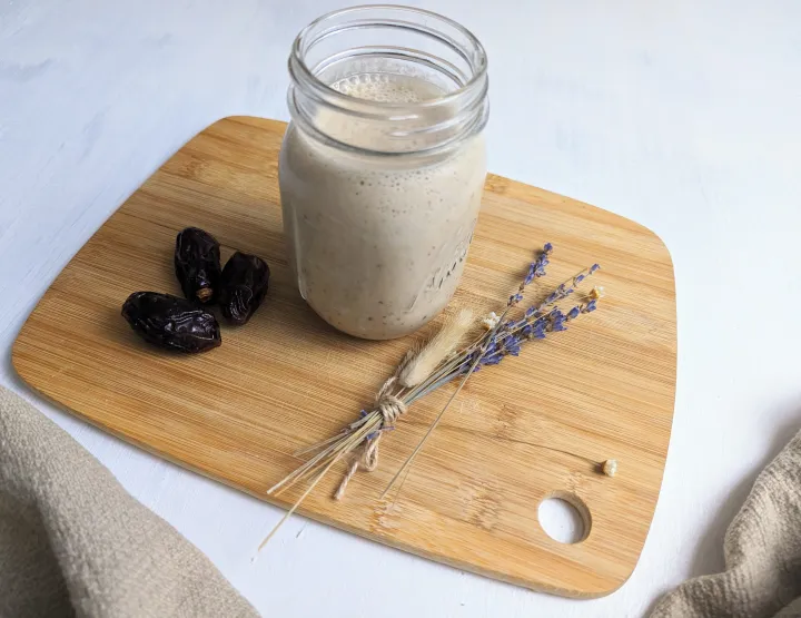 A smoothie in a mason jar, next to dates and flowers. 