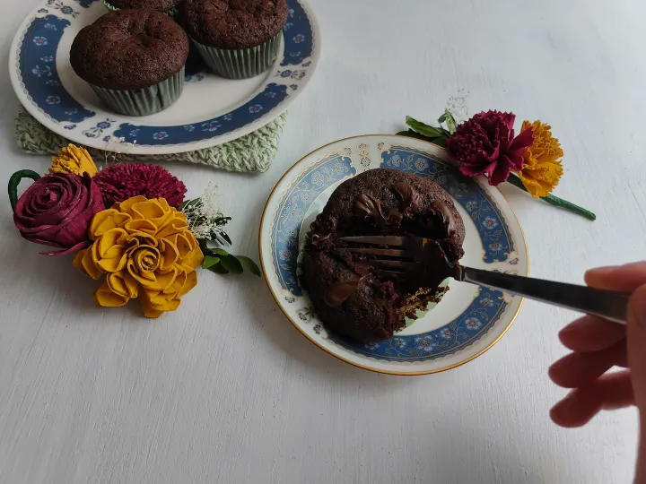 A chocolate muffin being cut with a fork, next to a plate full of more muffins