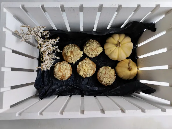 A wooden basket filled with zucchini muffins, pumpkins and flowers.