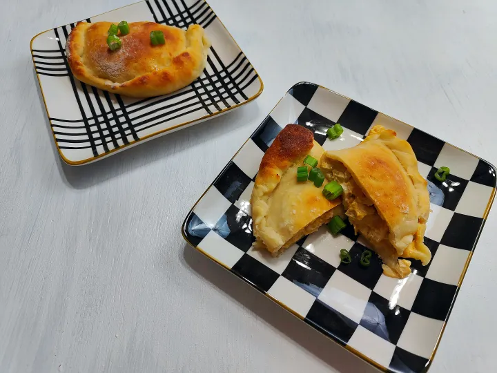 Buffalo chicken calzones on patterned plates, garnished with green onions