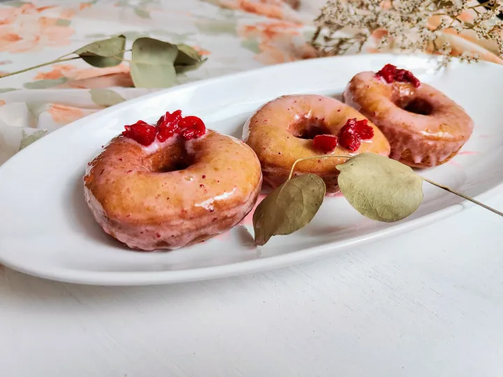 Three glazed strawberry donuts on a plate, topped with more strawberries